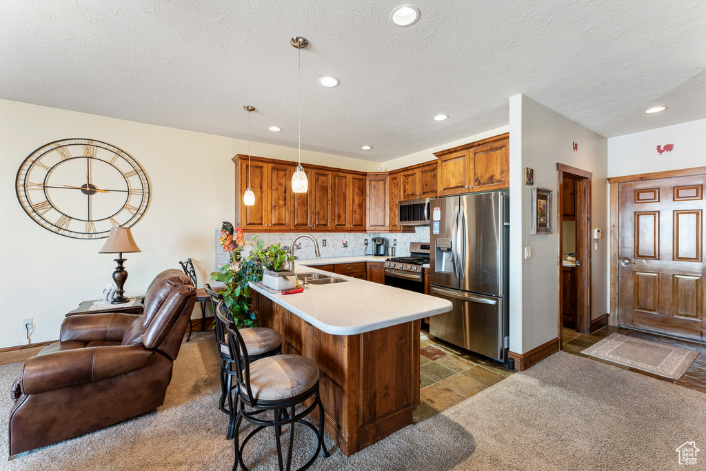 Kitchen with pendant lighting, sink, stainless steel appliances, a kitchen bar, and kitchen peninsula