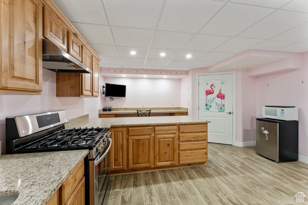 Kitchen featuring light stone counters, a paneled ceiling, stainless steel range with gas stovetop, and light hardwood / wood-style floors