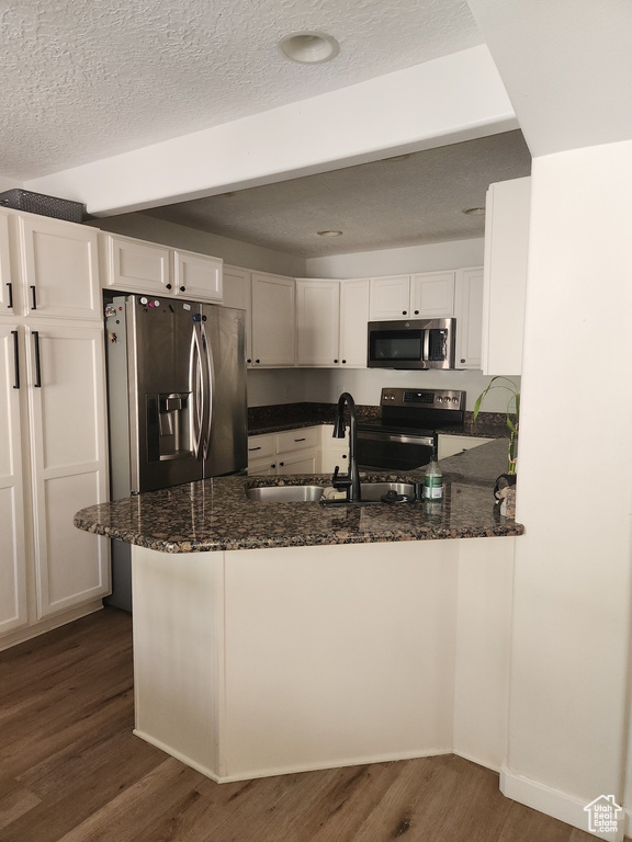 Kitchen featuring appliances with stainless steel finishes, dark wood-type flooring, dark stone counters, white cabinets, and a textured ceiling