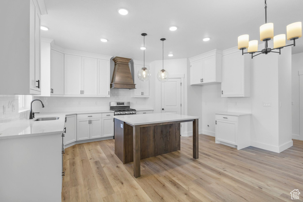 Kitchen featuring stainless steel range oven, white cabinetry, sink, hanging light fixtures, and custom range hood