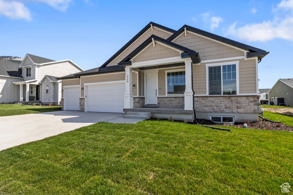 Craftsman house with driveway, a front lawn, an attached garage, and stone siding