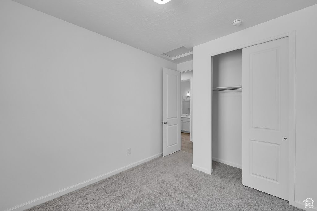 Unfurnished bedroom featuring light colored carpet, baseboards, attic access, a closet, and a textured ceiling