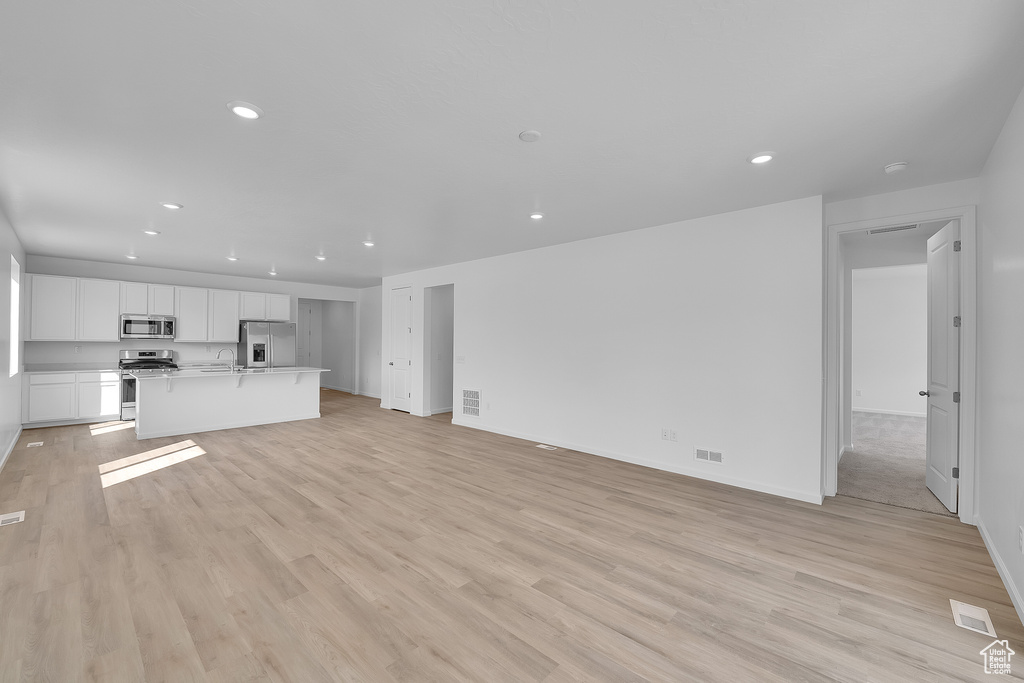 Unfurnished living room with recessed lighting, baseboards, light wood-style floors, and a sink