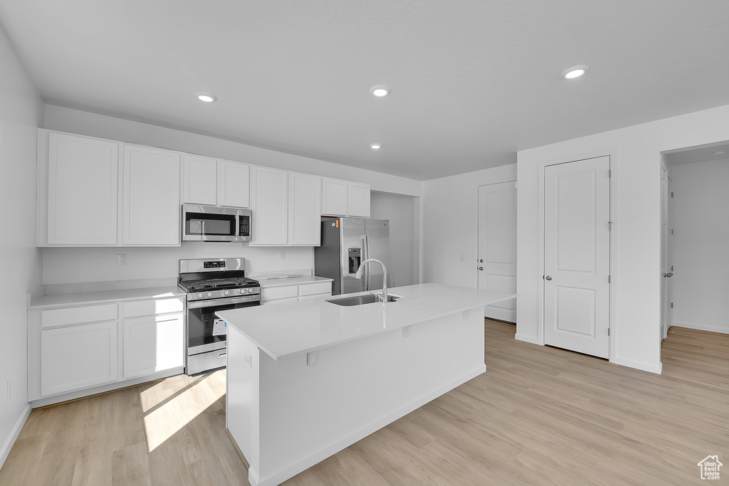 Kitchen with appliances with stainless steel finishes, a sink, white cabinetry, an island with sink, and baseboards