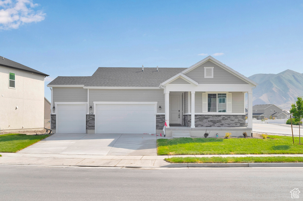 Craftsman inspired home featuring a garage, concrete driveway, a porch, a front lawn, and a mountain view