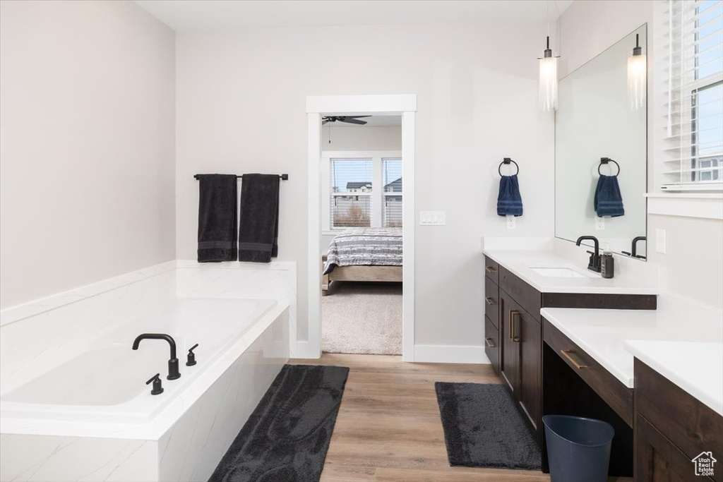 Bathroom with ceiling fan, a relaxing tiled tub, wood-type flooring, and vanity