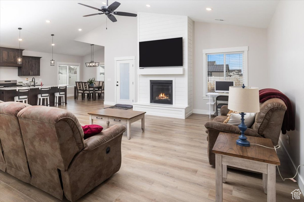 Living room with a fireplace, sink, vaulted ceiling, ceiling fan, and light hardwood / wood-style flooring