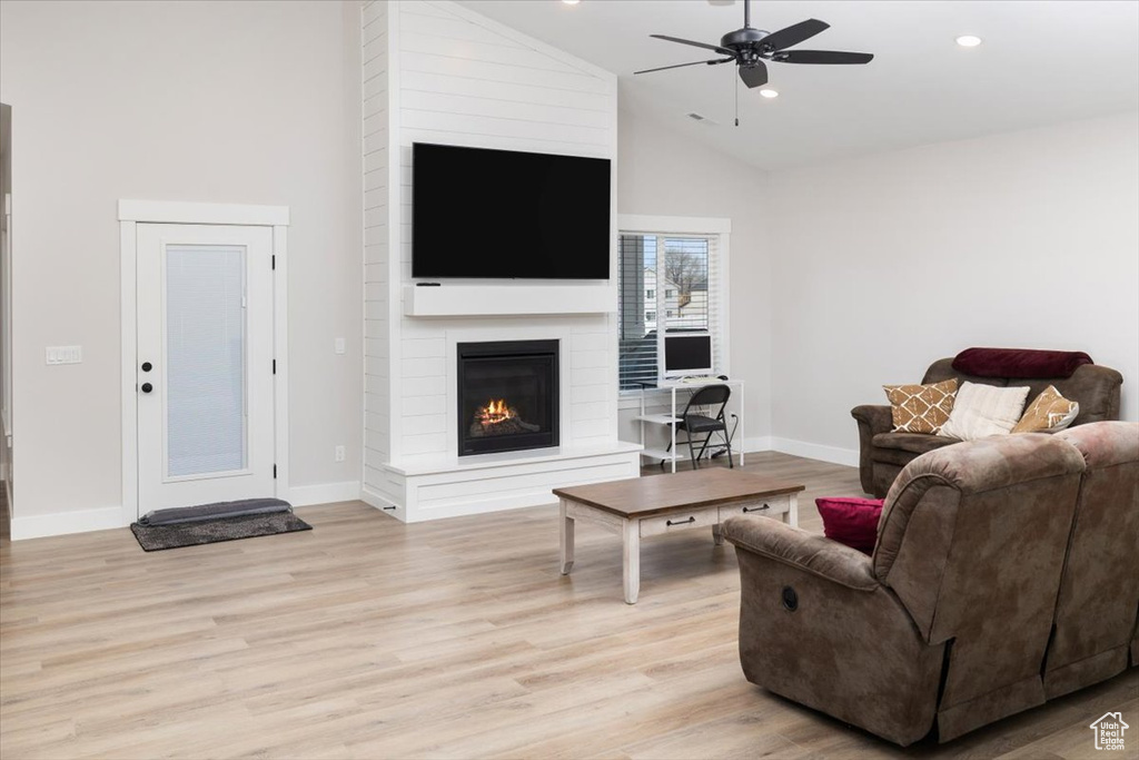 Living room featuring ceiling fan, high vaulted ceiling, a fireplace, and light hardwood / wood-style floors