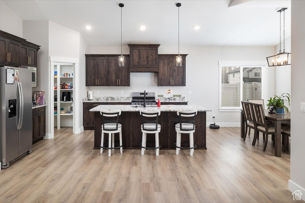 Kitchen with stainless steel appliances, dark brown cabinetry, a center island with sink, and hanging light fixtures