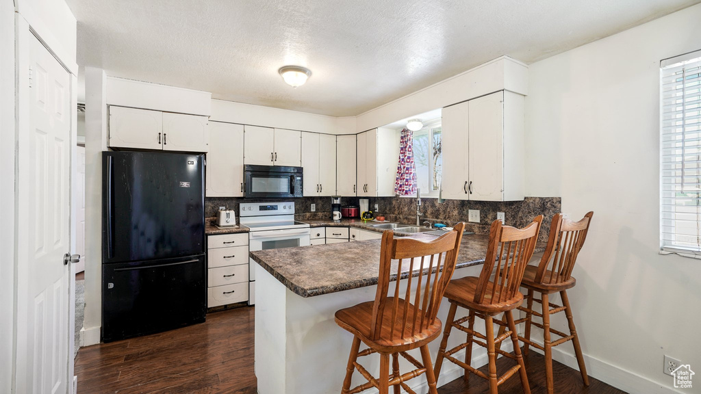 Kitchen with black appliances, white cabinets, kitchen peninsula, and a breakfast bar area