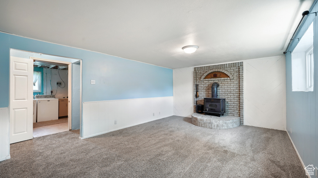 Unfurnished living room featuring washer / dryer, a wood stove, carpet floors, and a wainscoted wall