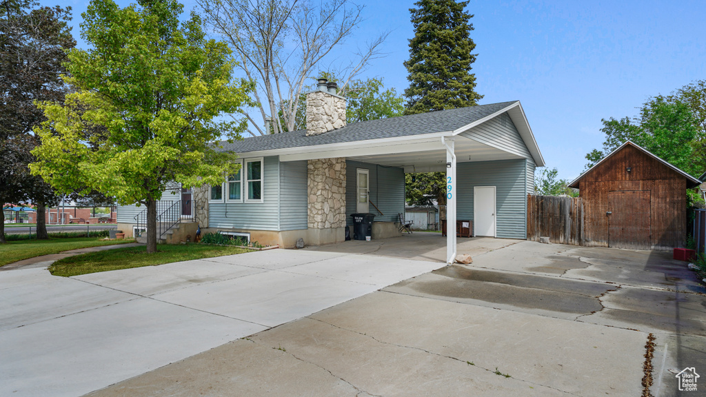 View of front facade featuring concrete driveway, a carport, a chimney, roof with shingles, and fence