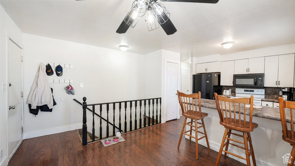 Kitchen with white cabinets, tasteful backsplash, dark hardwood / wood-style floors, black appliances, and a breakfast bar area