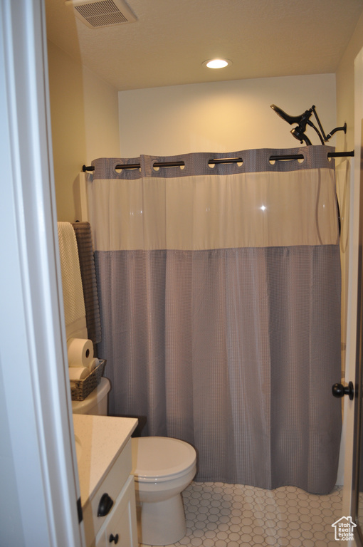 Bathroom with toilet, a shower with shower curtain, tile patterned flooring, and vanity