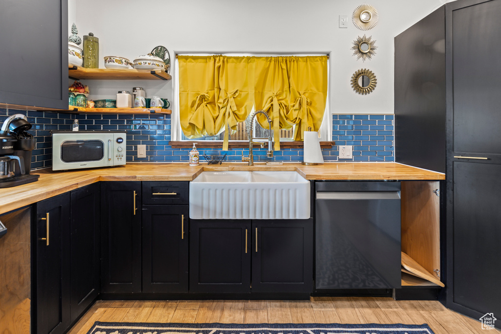 Kitchen with decorative backsplash, sink, black dishwasher, and butcher block counters