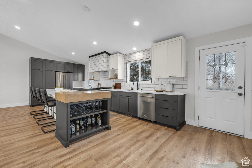 Kitchen with white cabinetry, light hardwood / wood-style floors, stainless steel appliances, lofted ceiling, and a kitchen island
