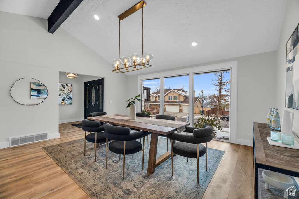 Dining area with vaulted ceiling with beams, an inviting chandelier, a textured ceiling, and light hardwood / wood-style flooring