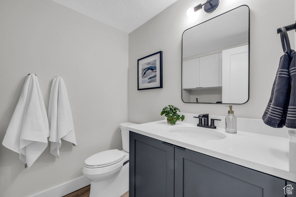 Bathroom with a textured ceiling, toilet, wood-type flooring, and vanity