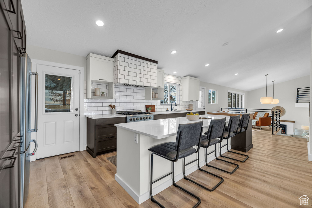 Kitchen with white cabinetry, light hardwood / wood-style floors, backsplash, lofted ceiling, and a center island