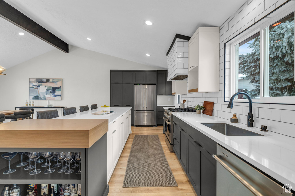 Kitchen featuring sink, appliances with stainless steel finishes, lofted ceiling with beams, and tasteful backsplash