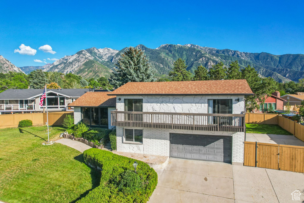 View of front of home with a front yard, fence, an attached garage, and a mountain view