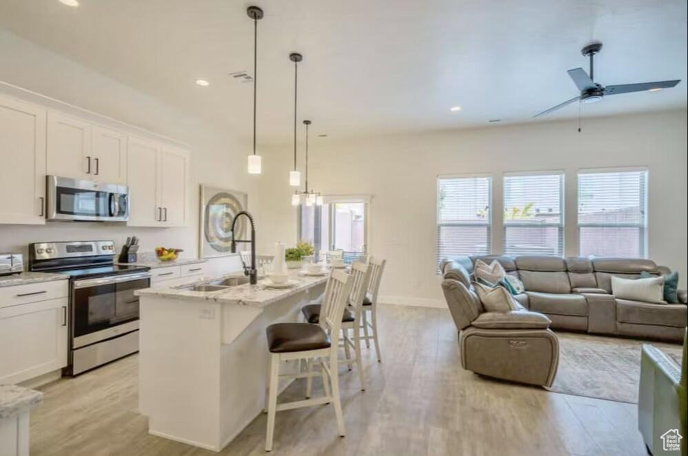 Kitchen with white cabinetry, a center island with sink, appliances with stainless steel finishes, pendant lighting, and sink
