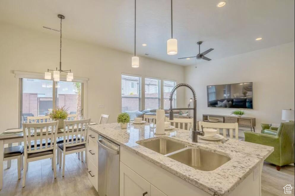 Kitchen with an island with sink, light stone countertops, pendant lighting, stainless steel dishwasher, and sink