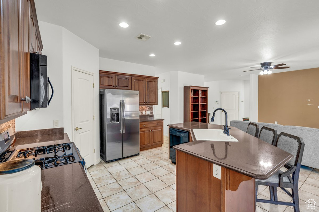 Kitchen featuring light tile patterned floors, a kitchen bar, a center island with sink, black appliances, and sink