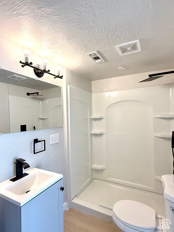 Bathroom featuring a textured ceiling, vanity, toilet, walk in shower, and hardwood / wood-style flooring