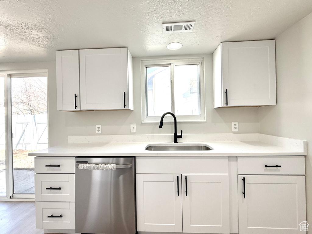 Kitchen with white cabinets, dishwasher, sink, and a textured ceiling