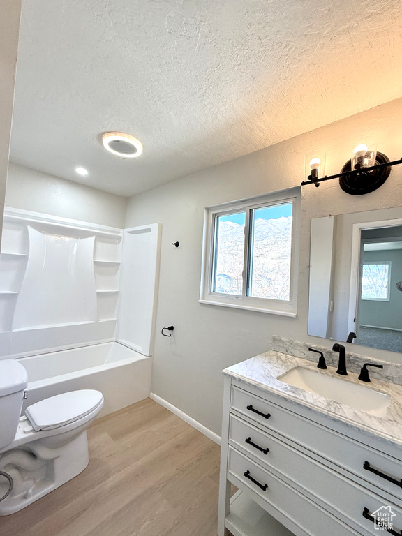 Full bathroom with toilet, hardwood / wood-style flooring, shower / washtub combination, a textured ceiling, and vanity