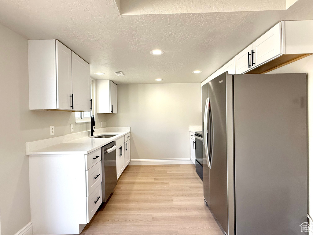 Kitchen featuring sink, light wood-type flooring, stainless steel appliances, a textured ceiling, and white cabinets