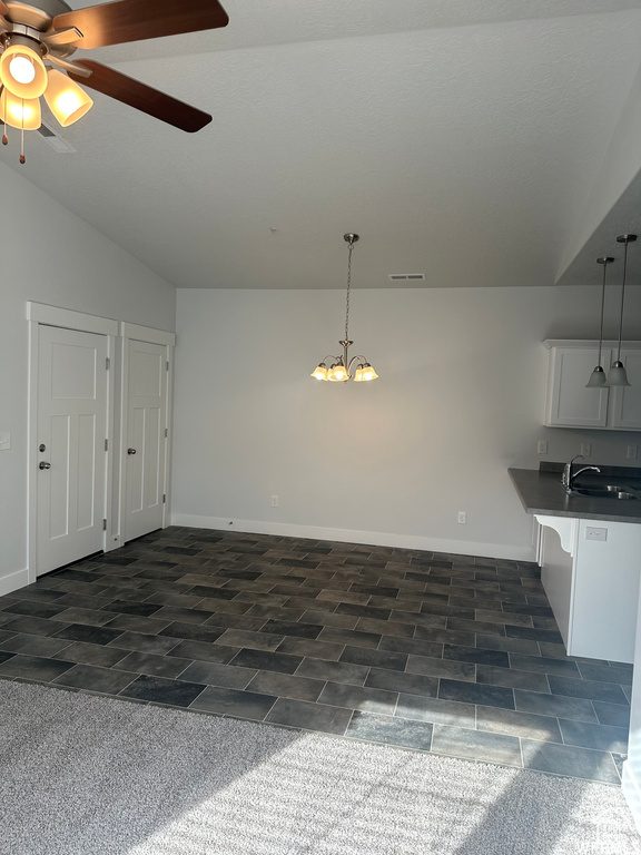 Unfurnished dining area with ceiling fan with notable chandelier, sink, and lofted ceiling