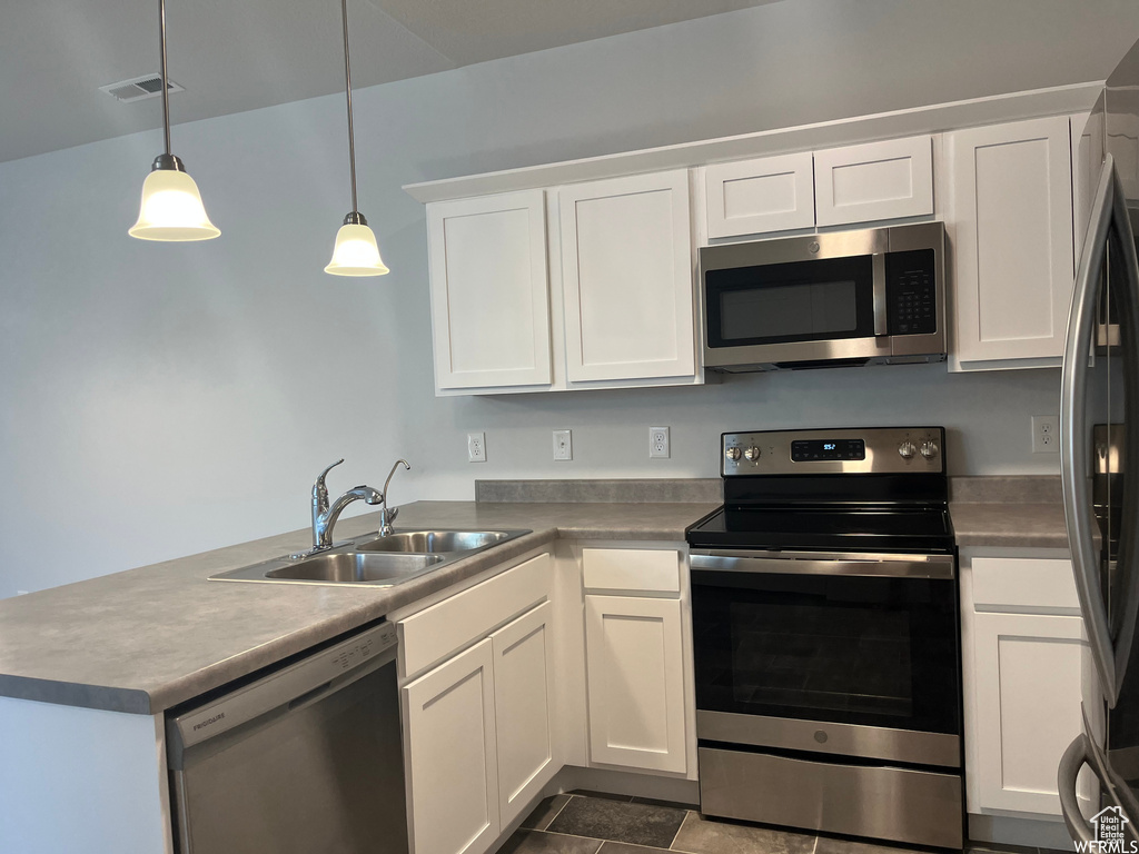 Kitchen featuring decorative light fixtures, kitchen peninsula, sink, white cabinetry, and stainless steel appliances