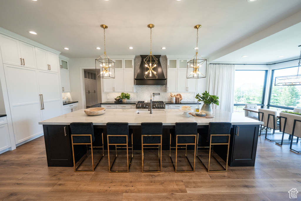 Kitchen with premium range hood, tasteful backsplash, a large island with sink, a breakfast bar, and white cabinets