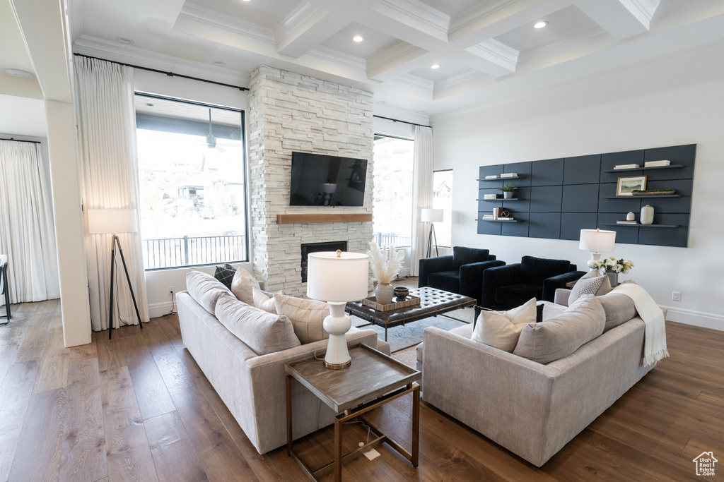 Living room featuring beam ceiling, crown molding, coffered ceiling, wood-type flooring, and a stone fireplace