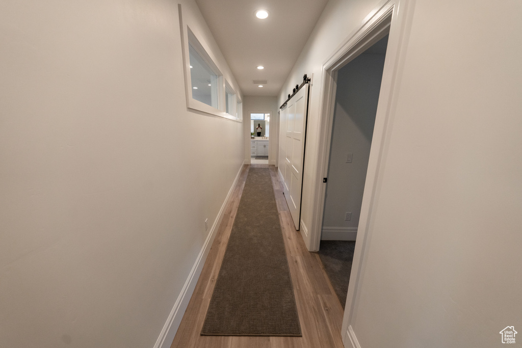 Hallway with a barn door, recessed lighting, and wood finished floors