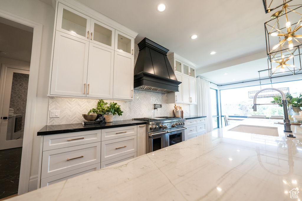 Kitchen with premium range hood, double oven range, a chandelier, dark stone countertops, and decorative backsplash