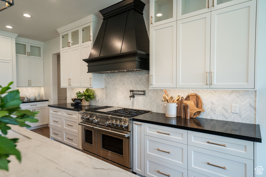 Kitchen featuring custom range hood, range with two ovens, white cabinets, decorative backsplash, and recessed lighting