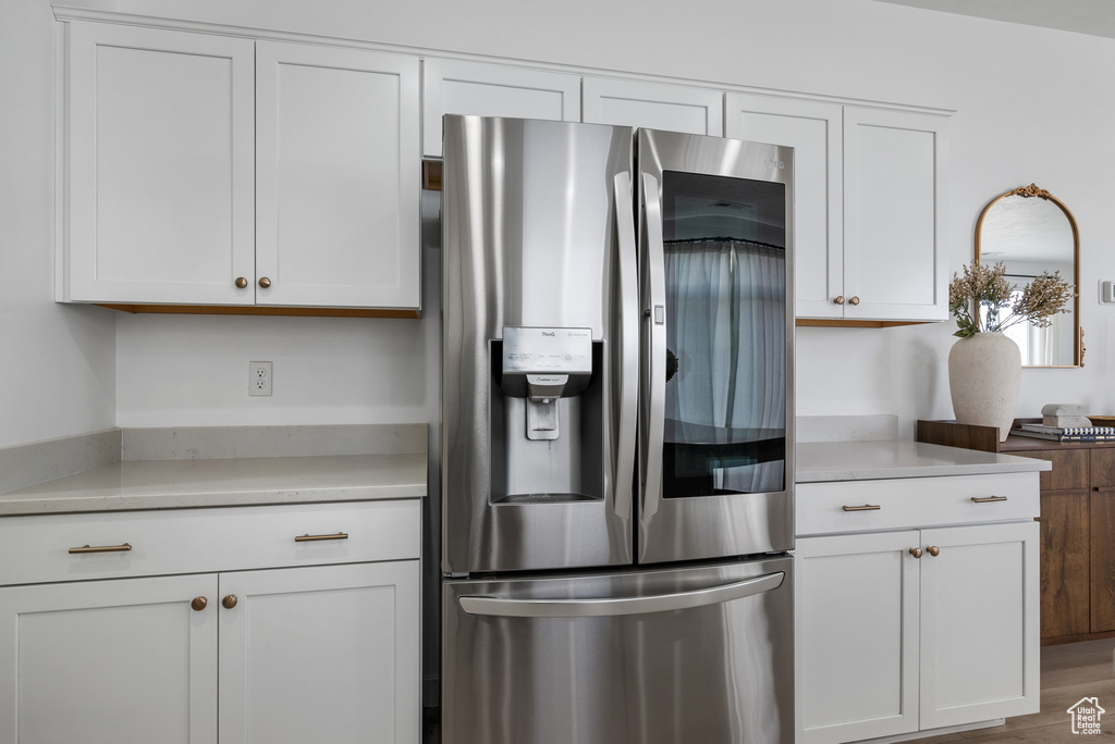 Kitchen with stainless steel fridge, hardwood / wood-style floors, and white cabinets