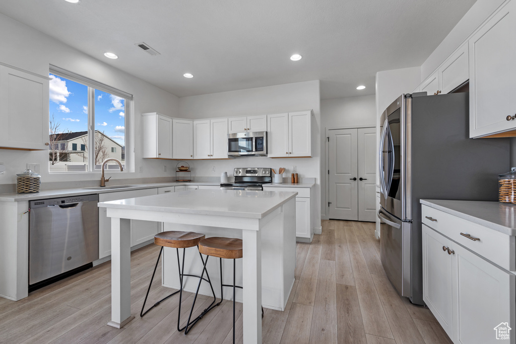 Kitchen with a breakfast bar, sink, white cabinets, a center island, and stainless steel appliances