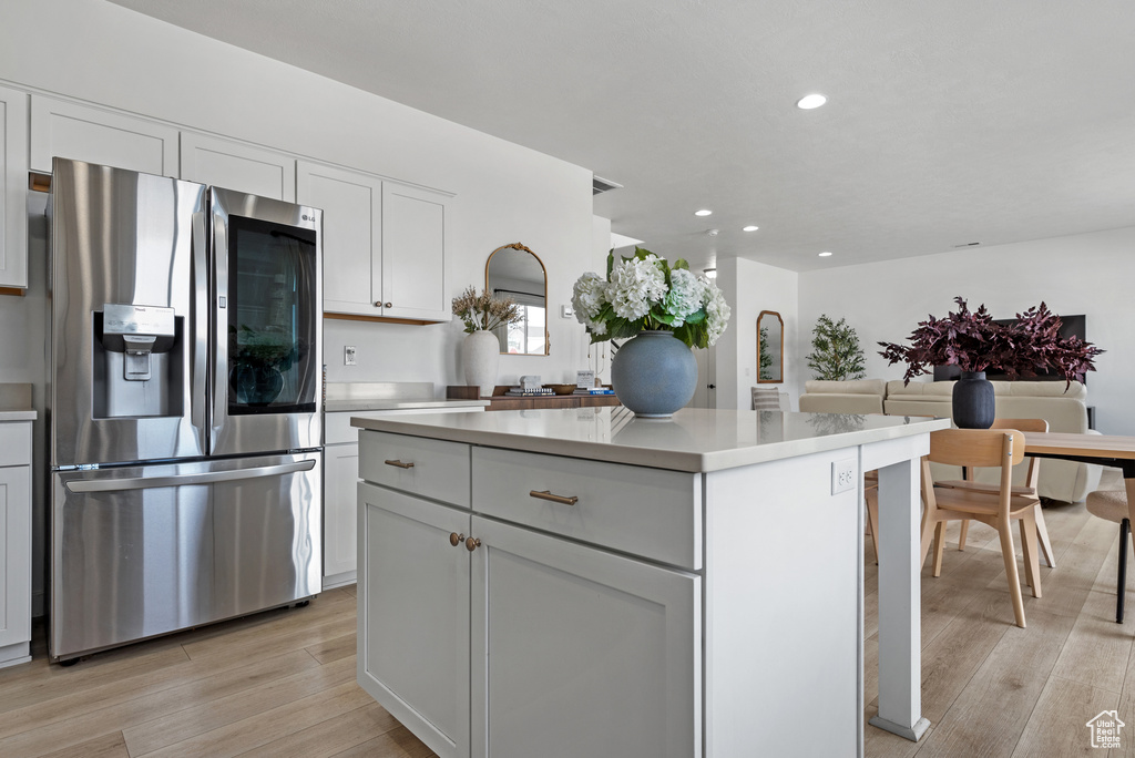Kitchen with stainless steel fridge, light wood-type flooring, a kitchen island, and white cabinets