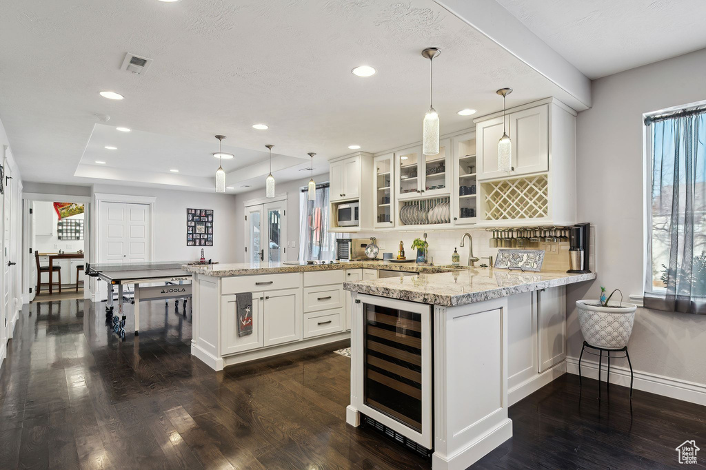 Kitchen featuring wine cooler, pendant lighting, kitchen peninsula, and white cabinets