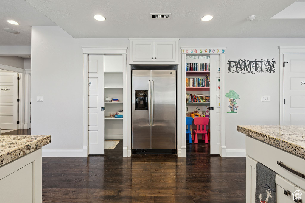 Kitchen featuring white cabinetry, light stone countertops, dark hardwood / wood-style floors, and stainless steel fridge