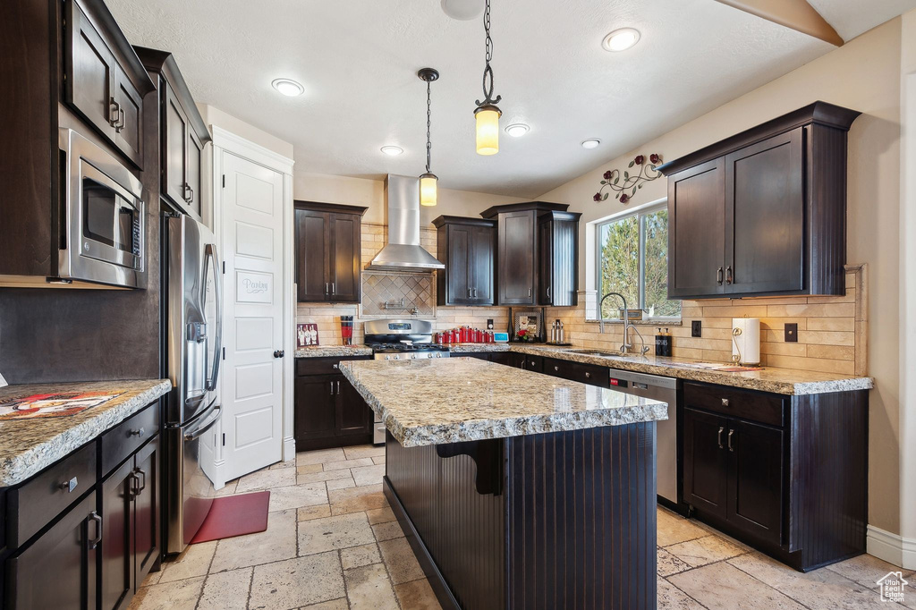 Kitchen with wall chimney exhaust hood, sink, decorative light fixtures, a center island, and stainless steel appliances