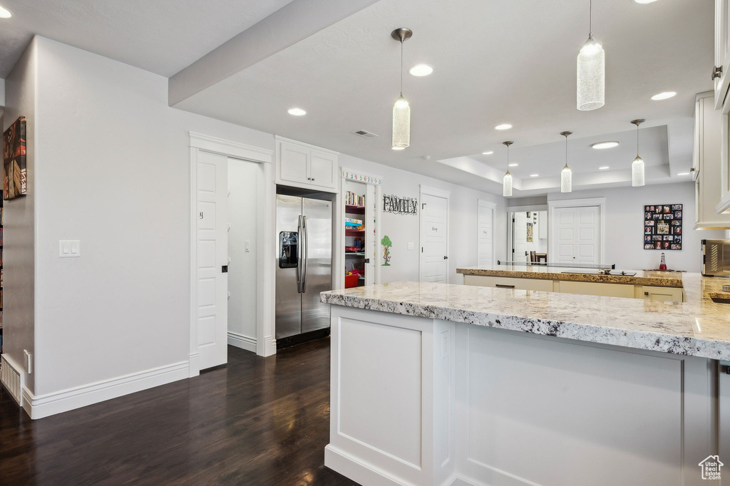 Kitchen with decorative light fixtures, stainless steel fridge with ice dispenser, a raised ceiling, light stone countertops, and white cabinets