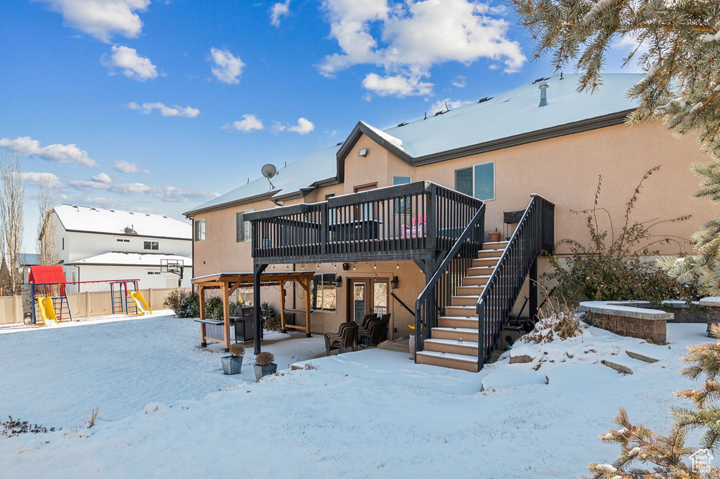 Snow covered property with a playground and a deck