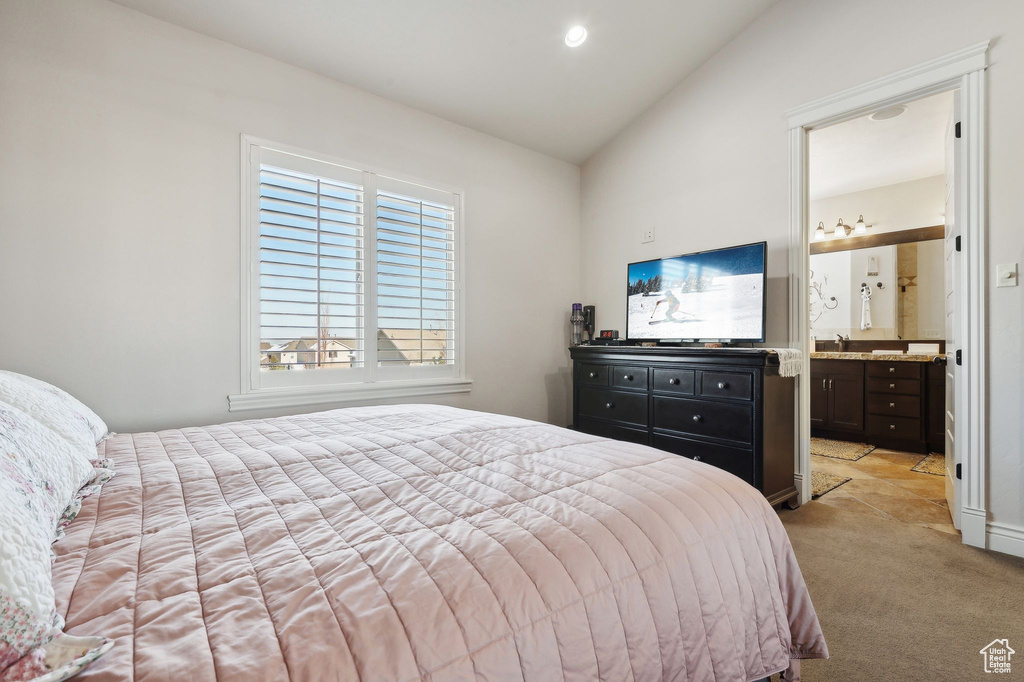 Bedroom with lofted ceiling, ensuite bathroom, sink, and light colored carpet