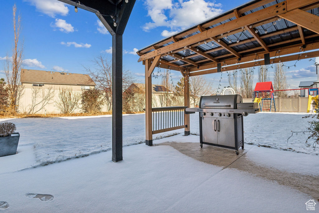 Snow covered patio featuring a playground and area for grilling