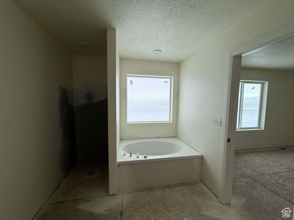 Bathroom with a bathtub, a textured ceiling, and a healthy amount of sunlight